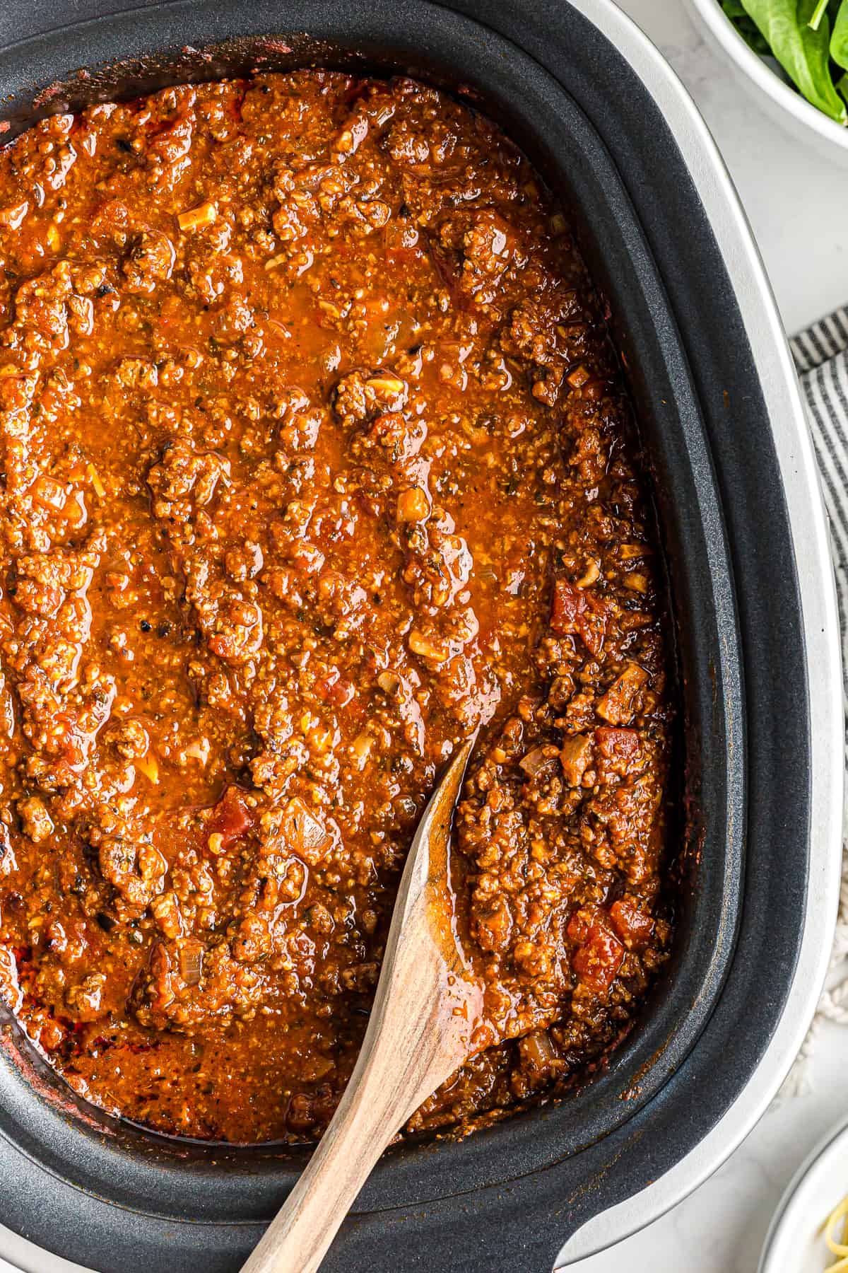 wooden spoon in spaghetti sauce in a crockpot.