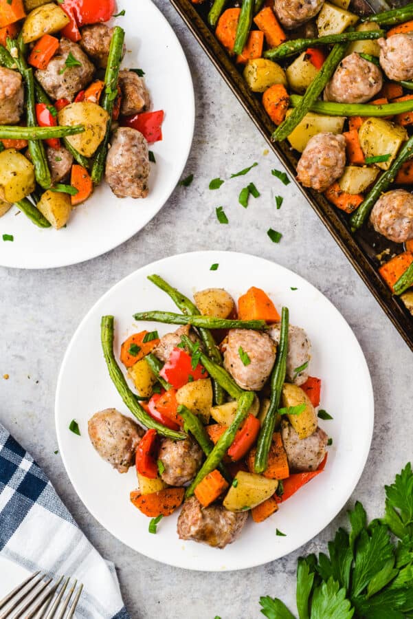 Sheet pan of sausage and veggies next to plates of food