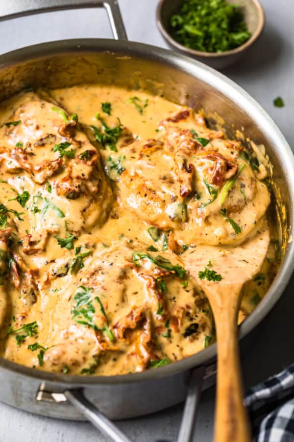 side shot of tuscan chicken in cream sauce with wooden spoon