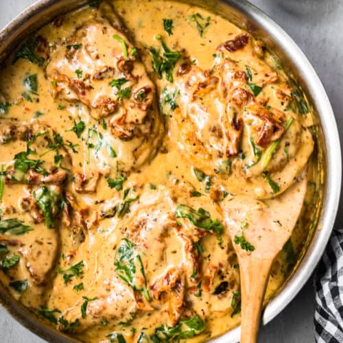 side shot of tuscan chicken in cream sauce with wooden spoon