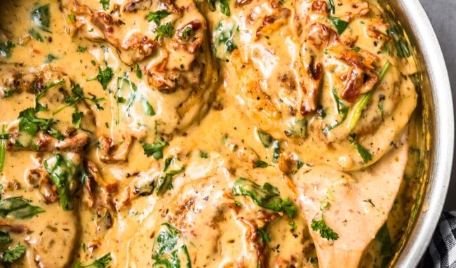 side shot of tuscan chicken in cream sauce with wooden spoon