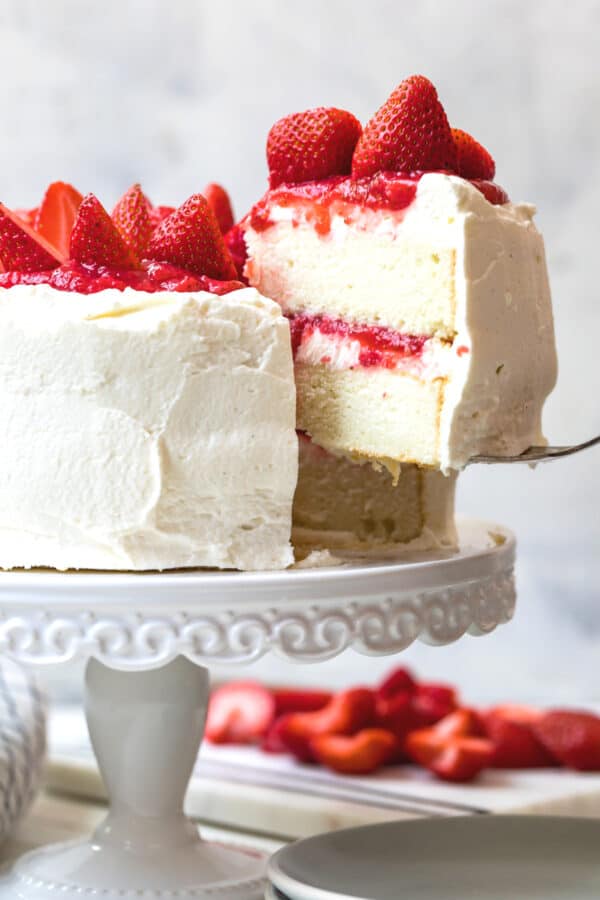 lifting slice of white layer cake with strawberry filling