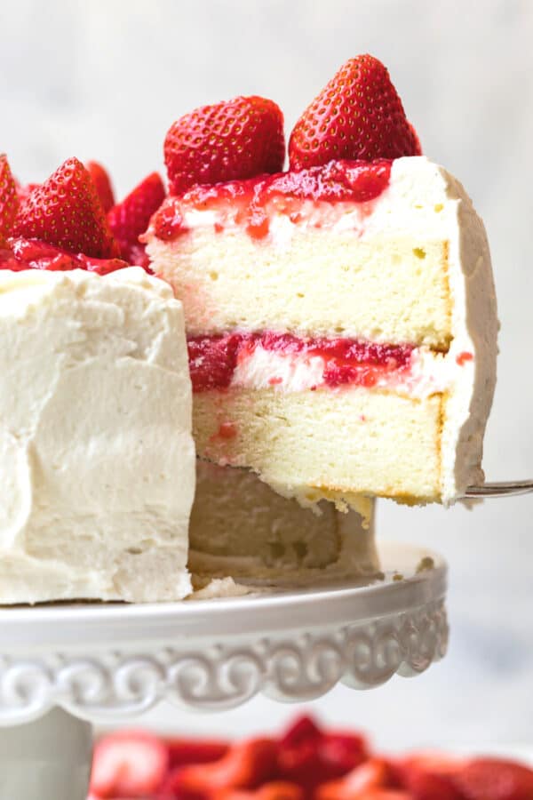 lifting slice of white layer cake with strawberry filling