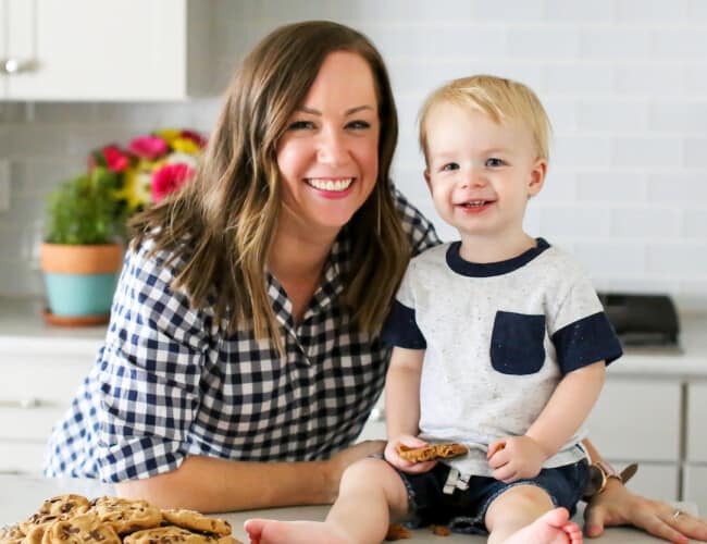 A food blogger posing with her baby in front of a kitchen counter.