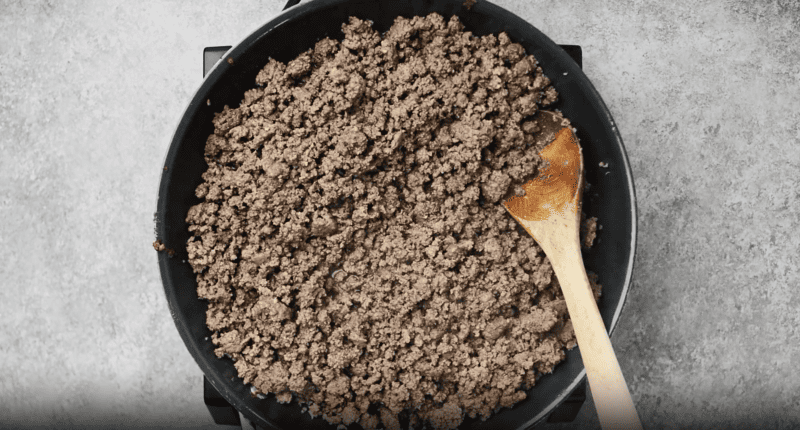 ground beef browning in a pan with a wooden spoon.