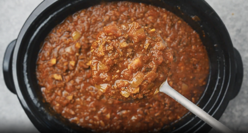 a spoonful of cooked meat sauce above a crockpot full of sauce.