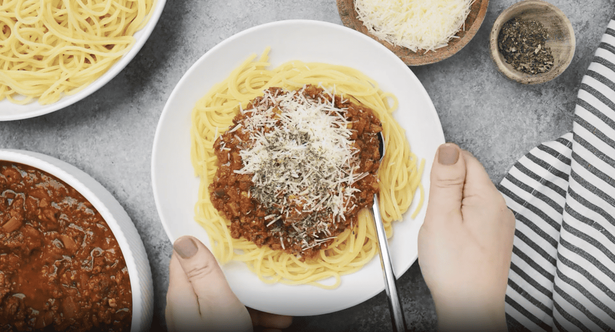 a serving of crockpot spaghetti sauce over pasta with cheese and basil on a white plate.