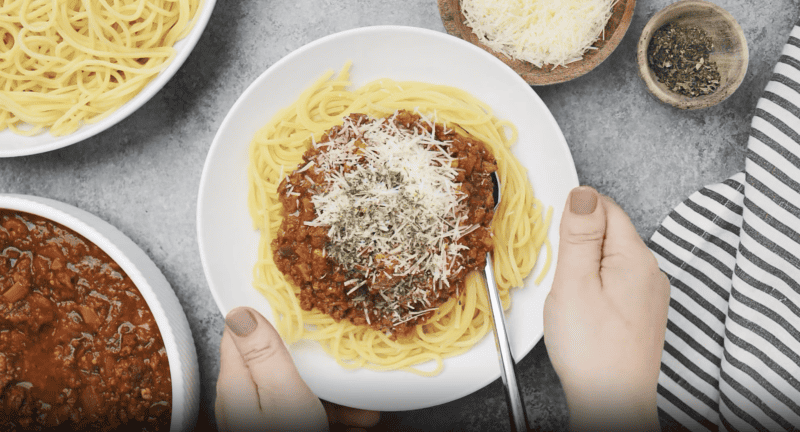 A person is holding a plate of spaghetti and meatballs topped with homemade crockpot spaghetti sauce.