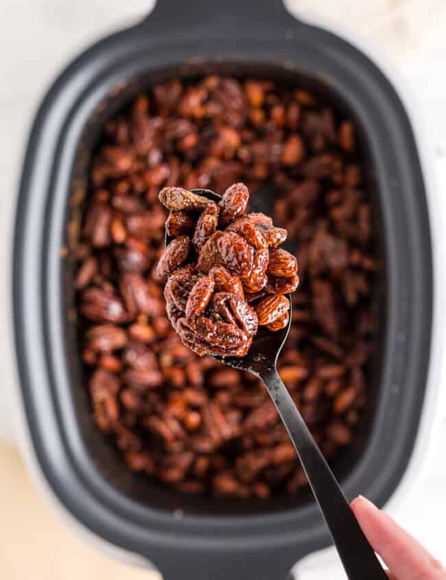 lifting up spoonful of crockpot candied nuts