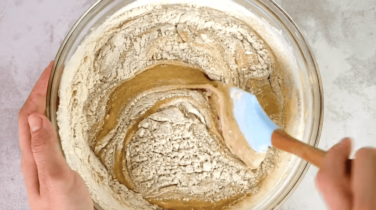 cake batter being mixed with a rubber spatula in a glass bowl.