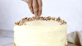 sprinkling chopped pecans over frosted carrot cake.