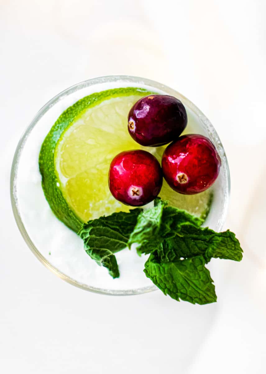 overhead image of coconut mojito with cranberries, mint, and lime