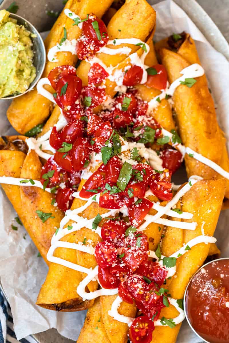 up close chicken taquitos on platter garnished with tomatoes