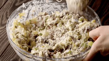 A person preparing Philly cheesesteak dip by squeezing meat into a bowl.