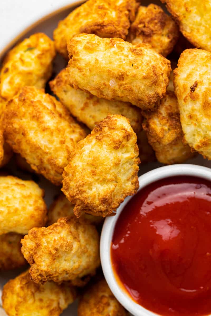 up close air fryer tater tots in white bowl with ketchup
