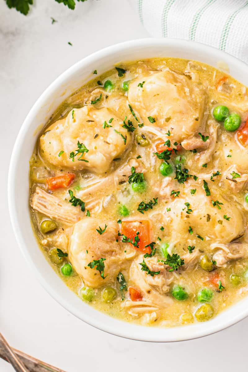 overhead image of bowl of crockpot chicken and dumplings garnished with parsley
