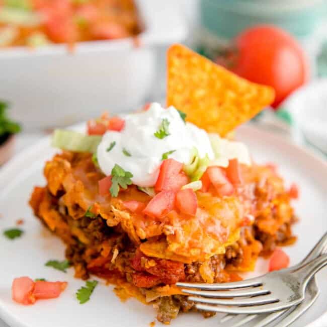 slice of dorito casserole garnished with sour cream and chopped tomatoes