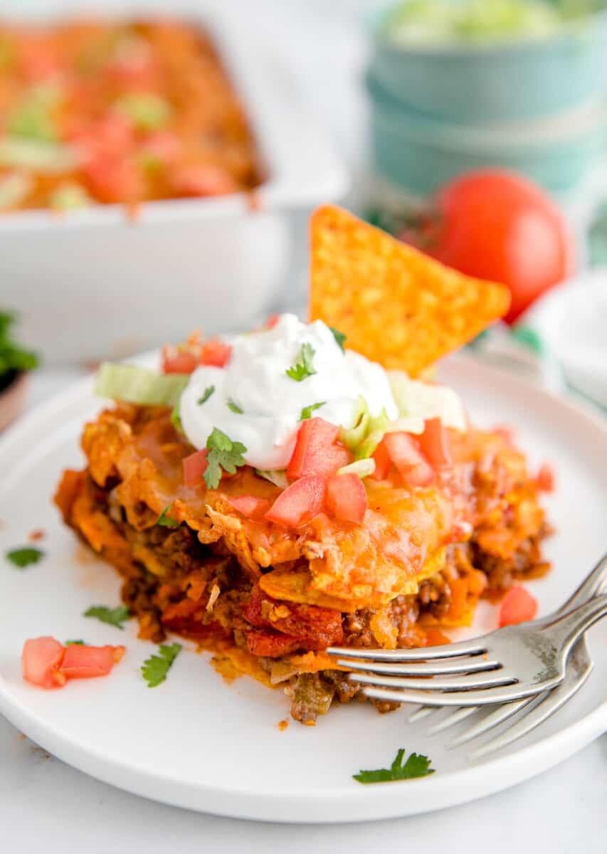 slice of dorito casserole garnished with sour cream and chopped tomatoes