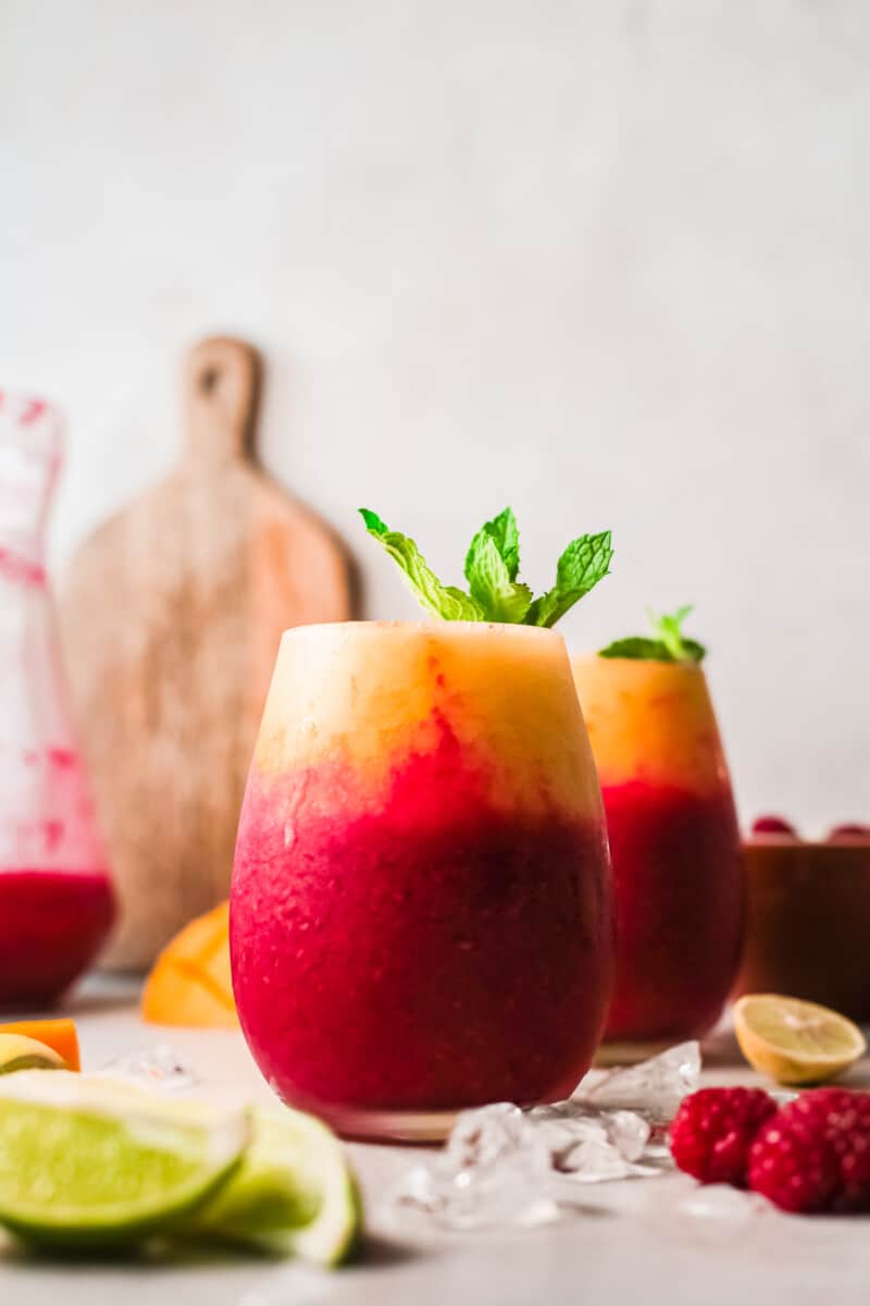 two glasses with layered raspberry mango daiquiris garnished with mint