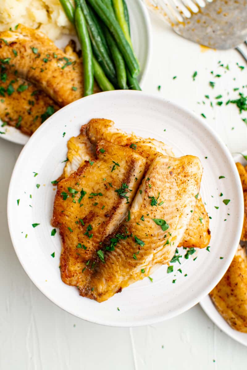 pan fried tilapia on white plates garnished with parsley