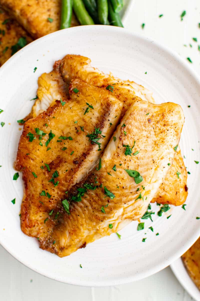 pan fried tilapia on white plates garnished with parsley