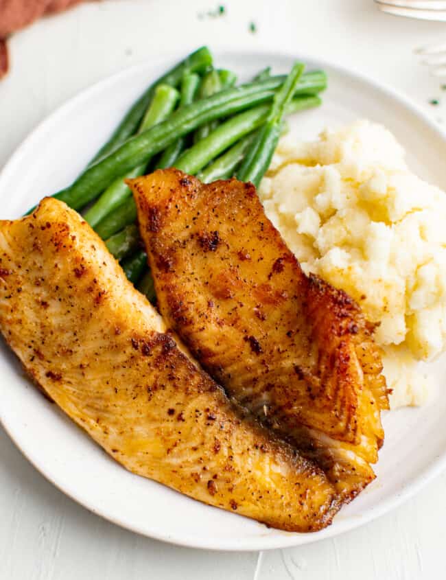 pan fried tilapia on plate with green beans and mashed potatoes