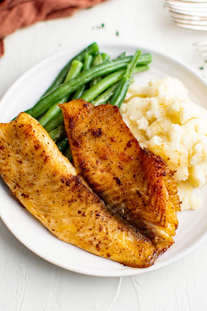 pan fried tilapia on plate with green beans and mashed potatoes