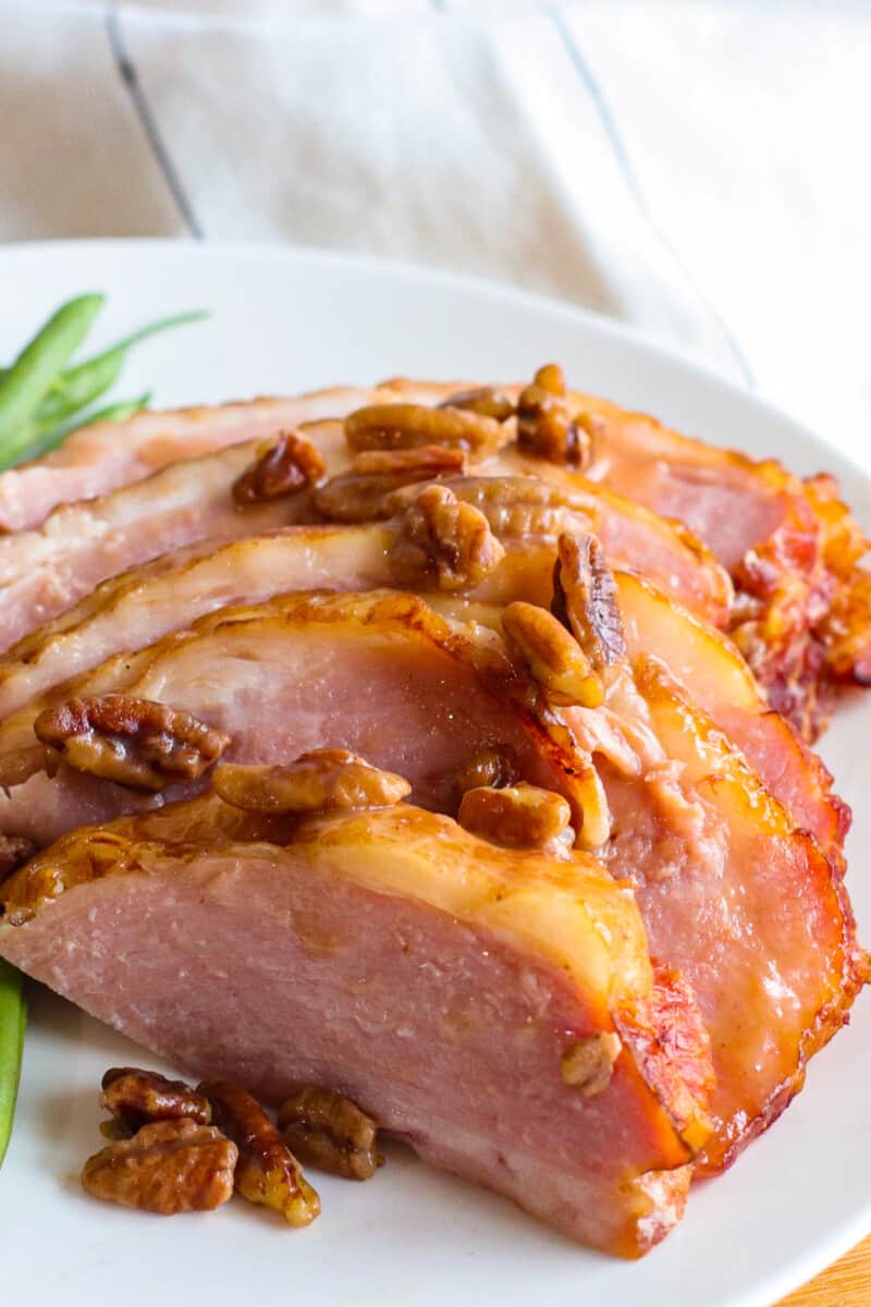 slices of pecan bourbon glazed ham on white plate with green beans