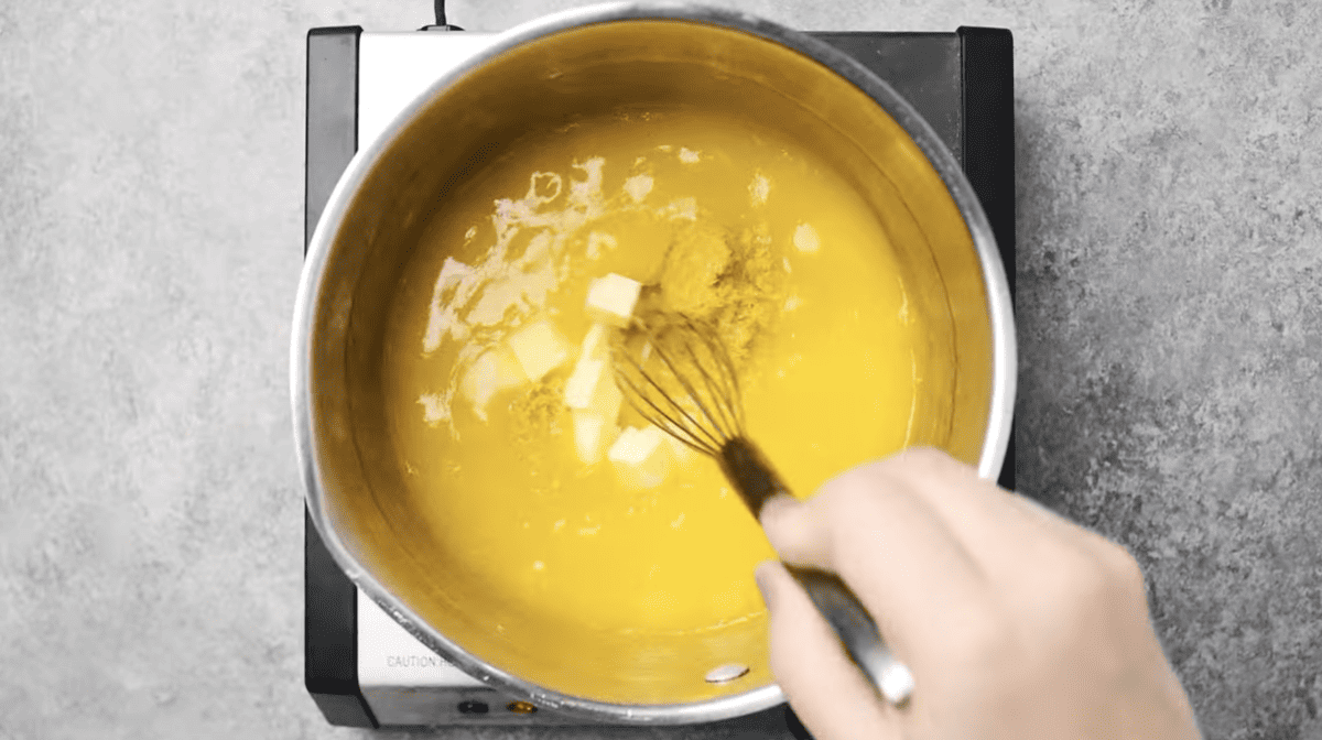 butter and lemon zest added to lemon curd in a saucepan with a whisk.