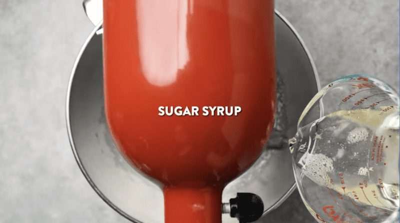 sugar syrup poured into egg whites in a red stand mixer.