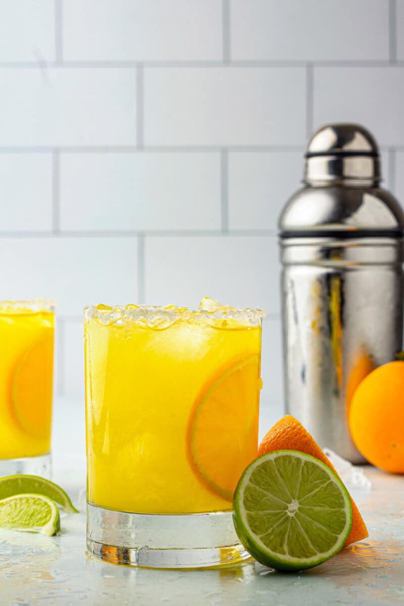 orange margaritas next to cocktail shaker