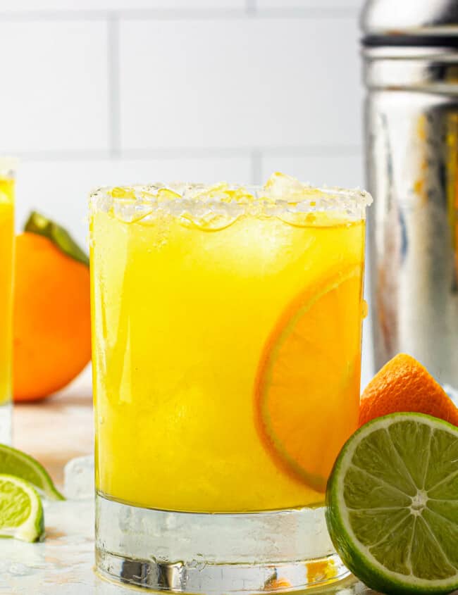 orange margarita next to cocktail shaker