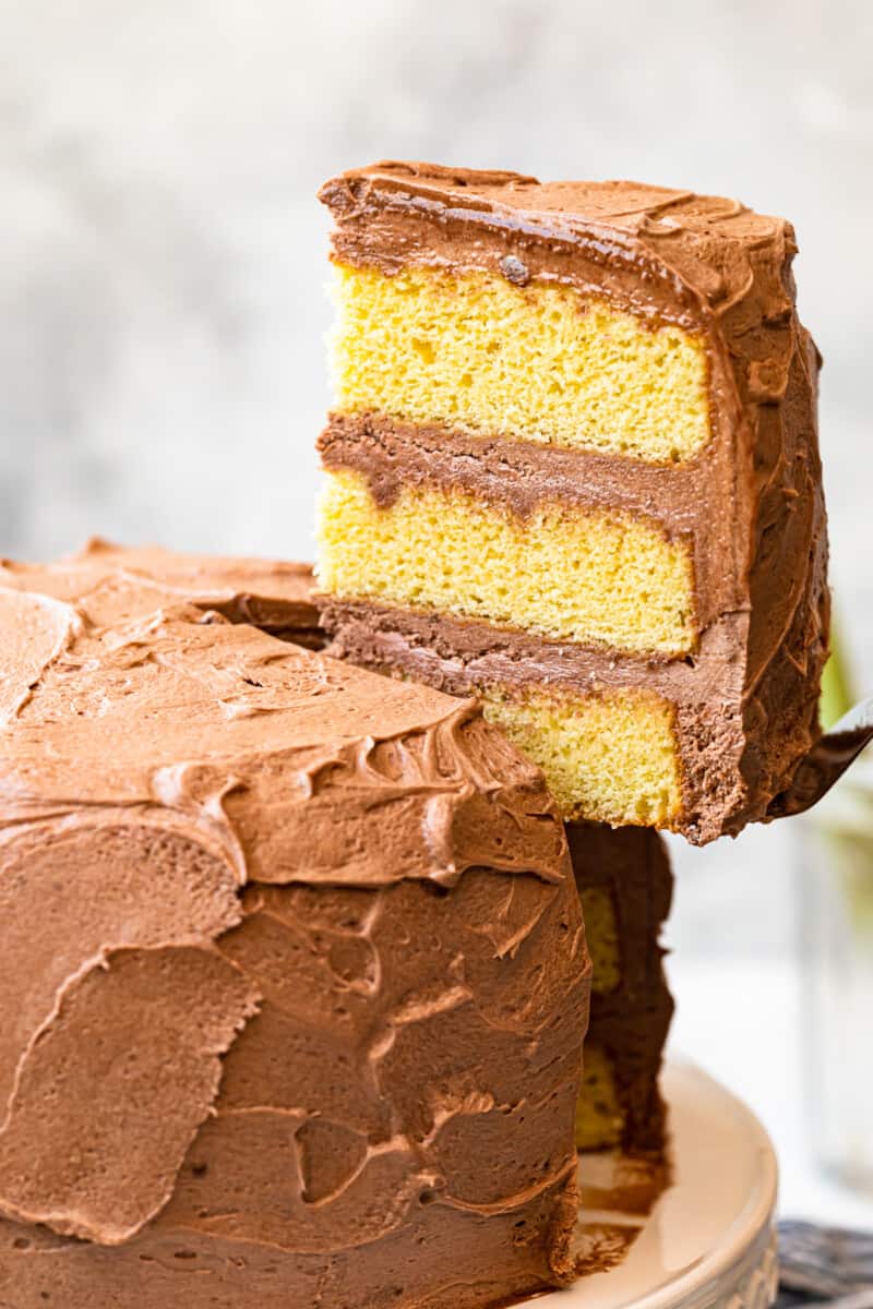 lifting up slice of yellow layer cake with milk chocolate frosting