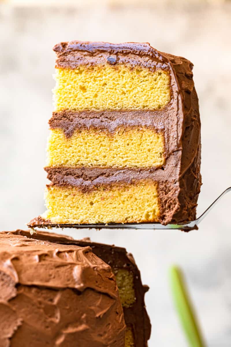 lifting up slice of yellow layer cake with milk chocolate frosting