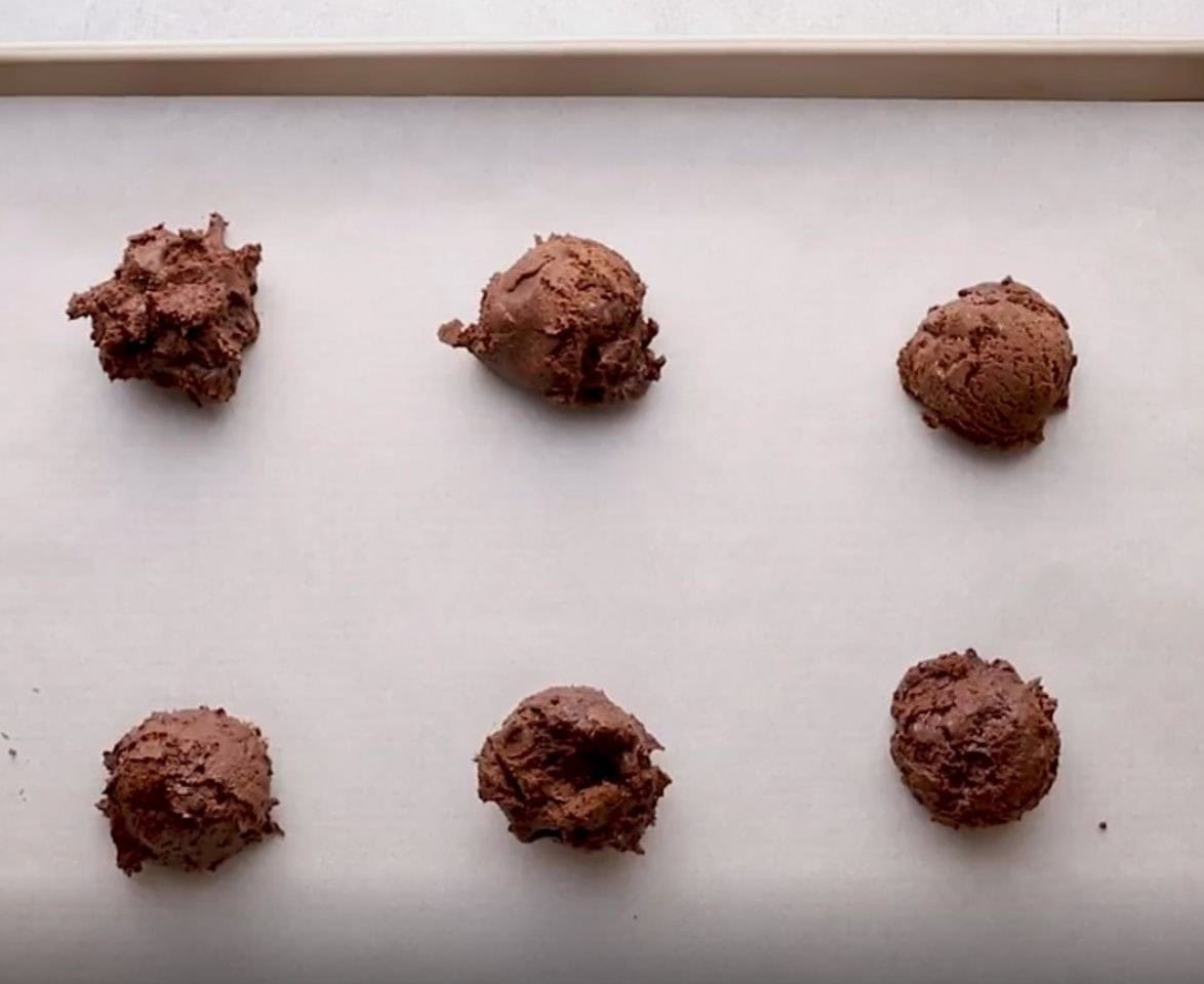 Brownie cookie batter in balls on a lined cookie sheet.  - 8