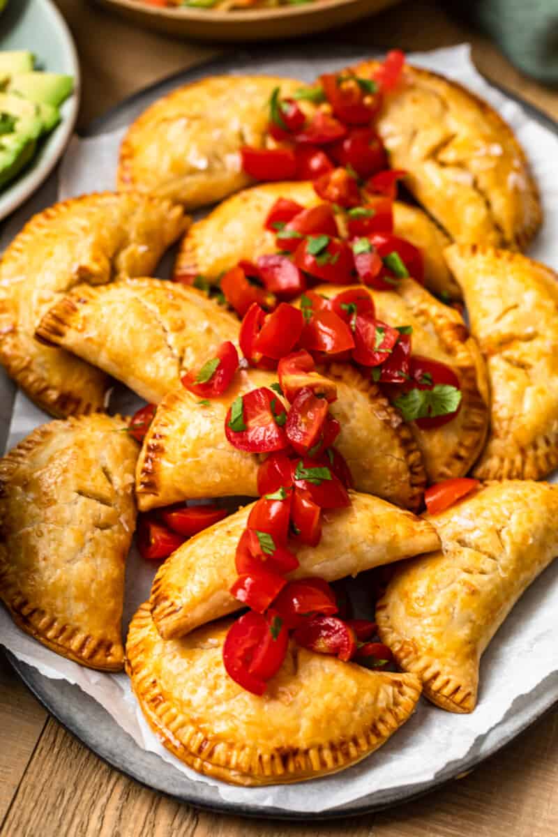 baked chicken empanadas on platter garnished with tomatoes