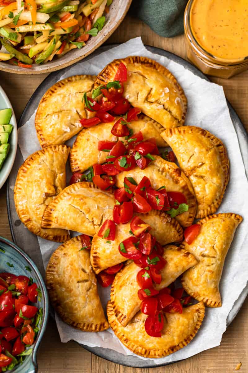 overhead baked chicken empanadas on platter garnished with tomatoes