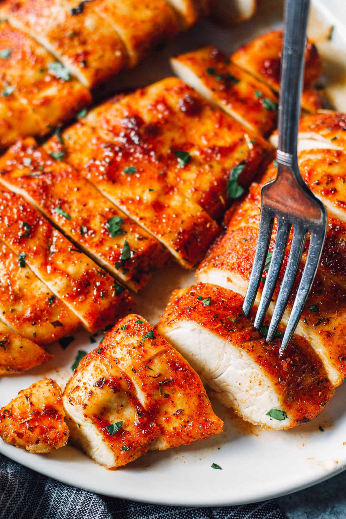 baked chicken breasts sliced on white platter with fork