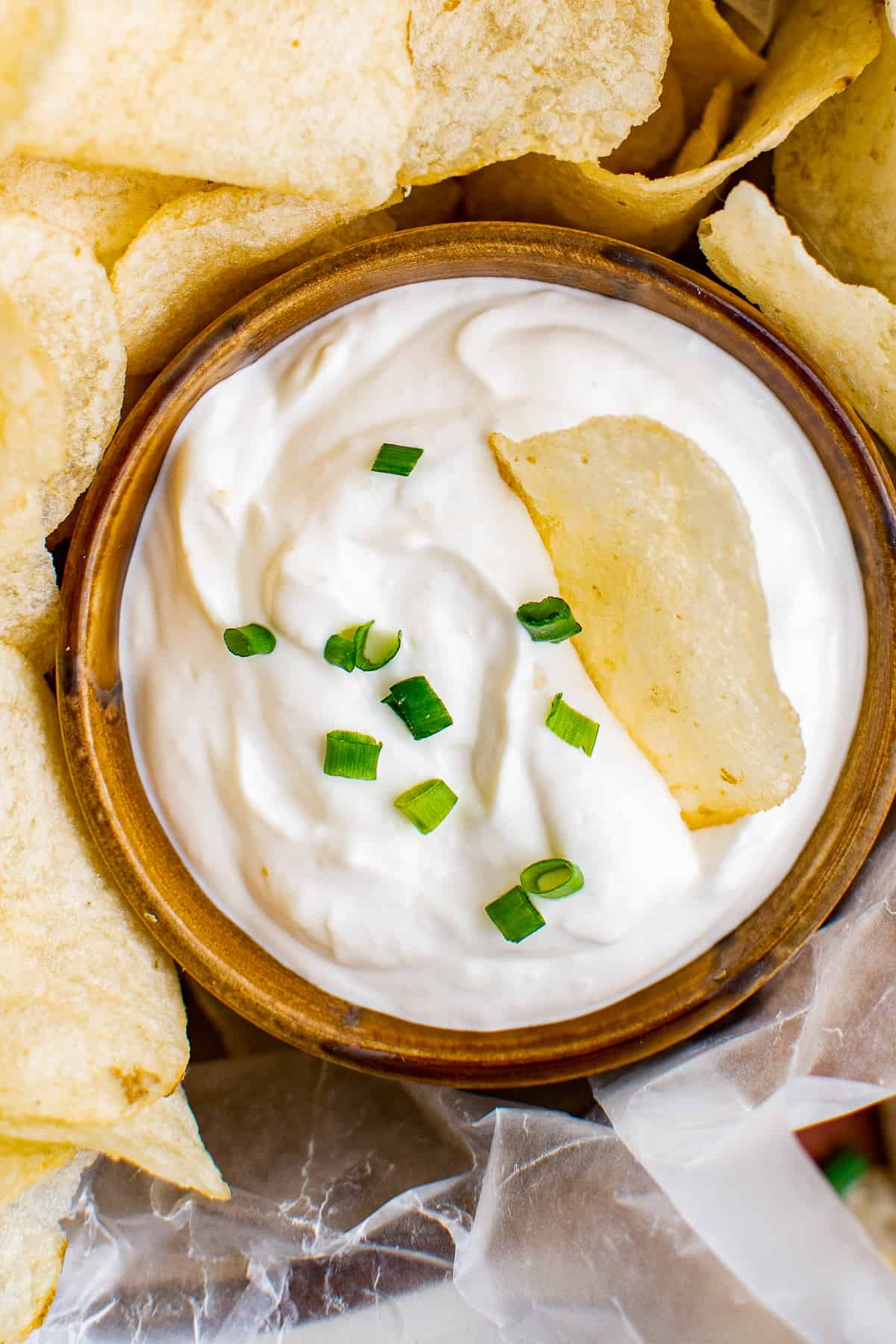 up close sour cream and onion dip in a bowl garnished with chives and chips.