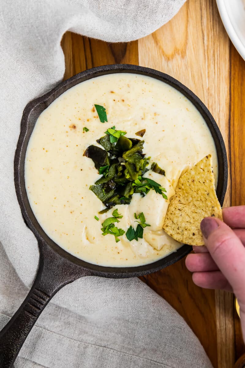 chip in spicy poblano queso in small cast iron skillet
