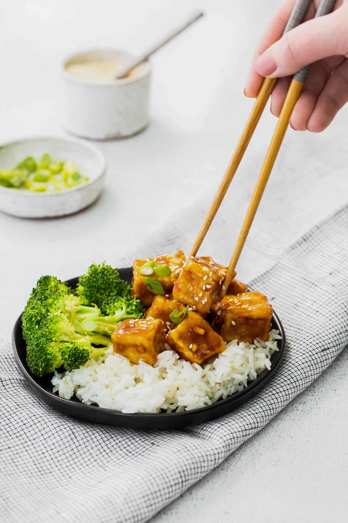 chopsticks grabbing a cube of air fryer teriyaki tofu on a black plate.