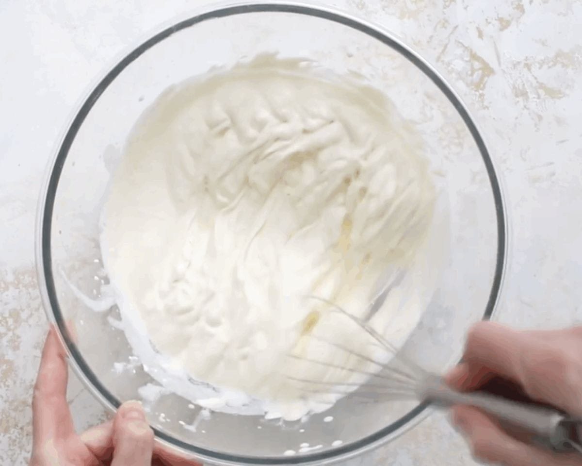 Whipping heavy cream with a whisk in a glass bowl.