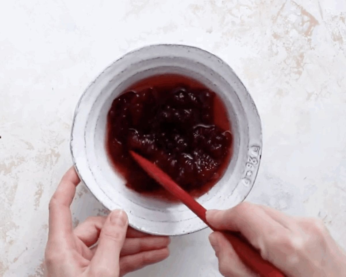 Stirring jam with Chambord in a white bowl with a red whisk.