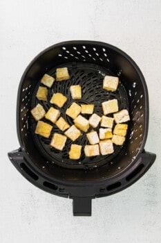 cubes of cooked air fryer teriyaki tofu in an air fryer basket.