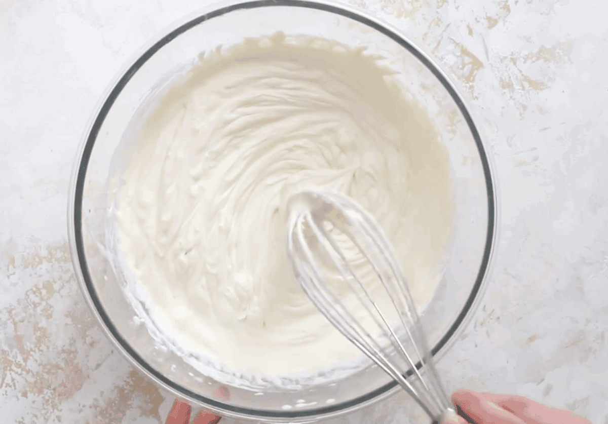 A bowl of fluffy, whipped mascarpone cream being mixed with a whisk, ready to be layered into the tiramisu.