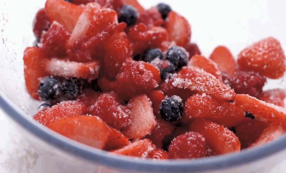 A bowl of macerated fresh strawberries, raspberries, and blueberries coated with sugar, ready to be layered into the dessert.