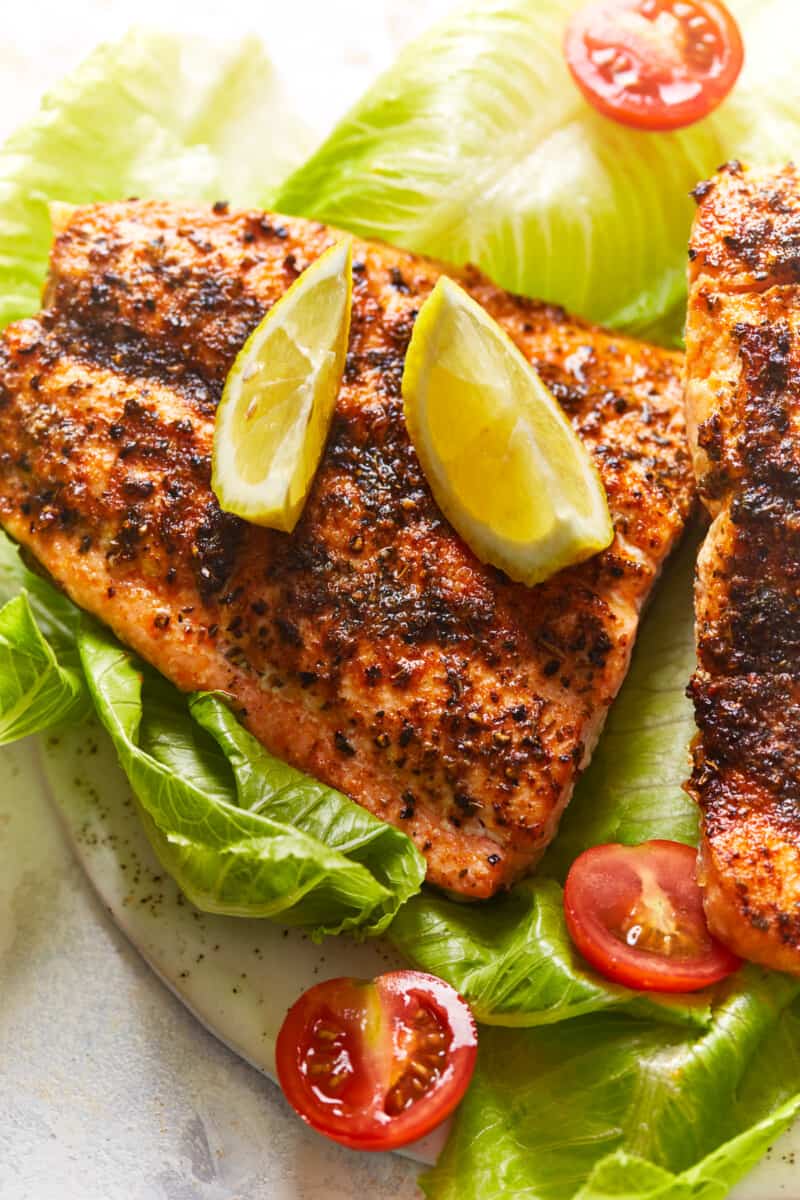 overhead view of an air fryer salmon filet on a bed of lettuce topped with lime wedges.