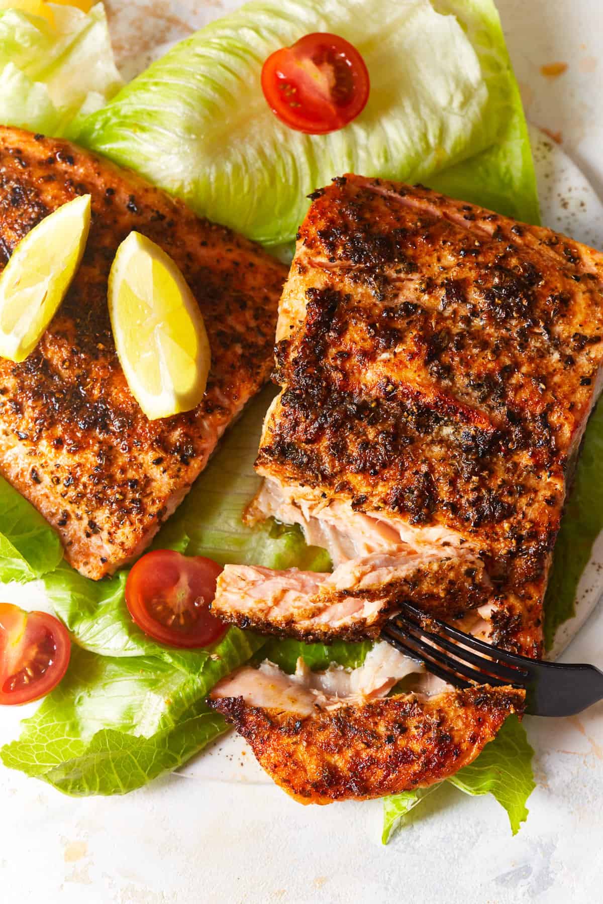 overhead view of 2 pieces of air fryer salmon on a bed of lettuce, one piece is being cut by a fork.