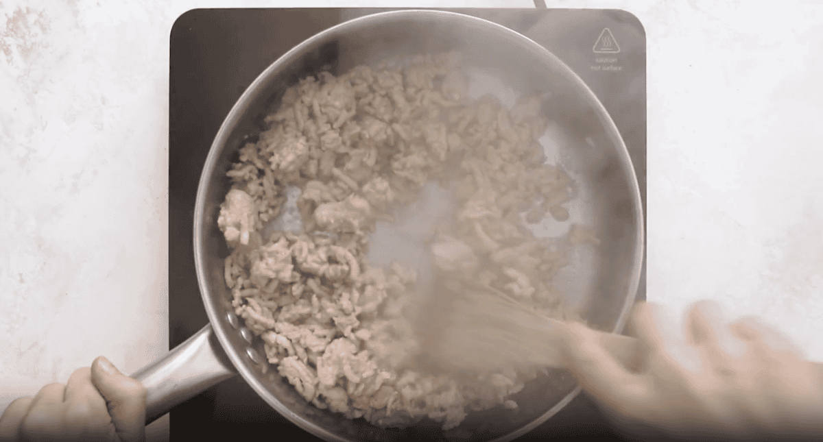 turkey cooking in a pan with a wooden spoon.