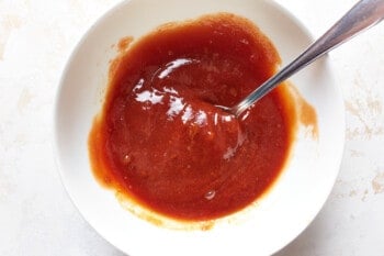 ketchup, brown sugar, mustard, and worcestershire sauce mixed together in a white bowl with a spoon.